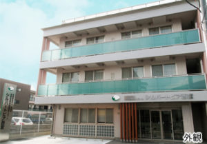 3階建ての介護施設の建物外観。白とグリーンの配色が特徴的な、モダンな居宅型施設。